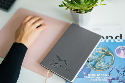 Notizbuch und beyond, das Magazin der Berlin University Alliance, auf einem Schreibtisch